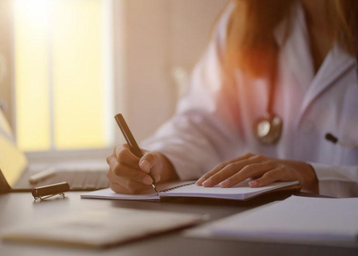 Close-up view of young female doctor writing medical charts with tablet in her office room