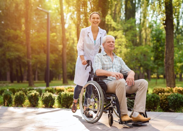 Doctor with old man in wheelchair walking in sunny park