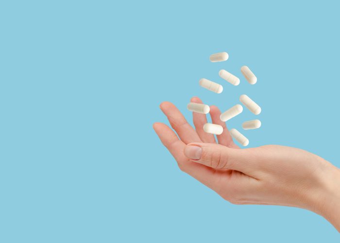 White pills floating over female hand isolated on blue. Healthcare and treatment concept. Copy space